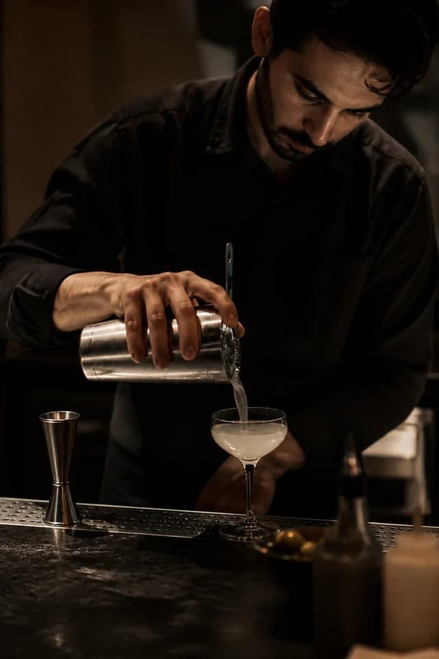 Imagem conceitual gerada por IA: bartender serve um cocktail sob iluminação baixa.